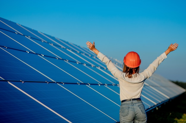 Beautiful young engineer standing near solar panels outdoors, Green Energy Concept.