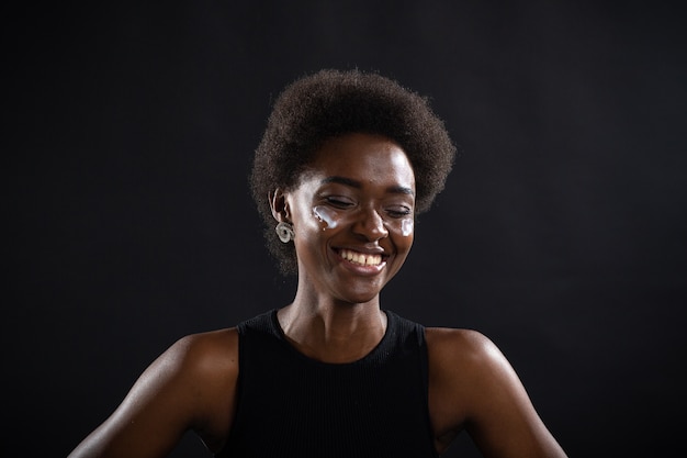 Beautiful young ethnic african american black woman applying moisturizer white cream on her face