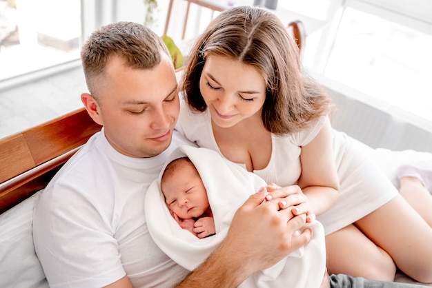 Bella giovane famiglia con figlia appena nata a letto con la luce del giorno. adorabile neonata che dorme nelle mani di sua madre e suo padre a casa