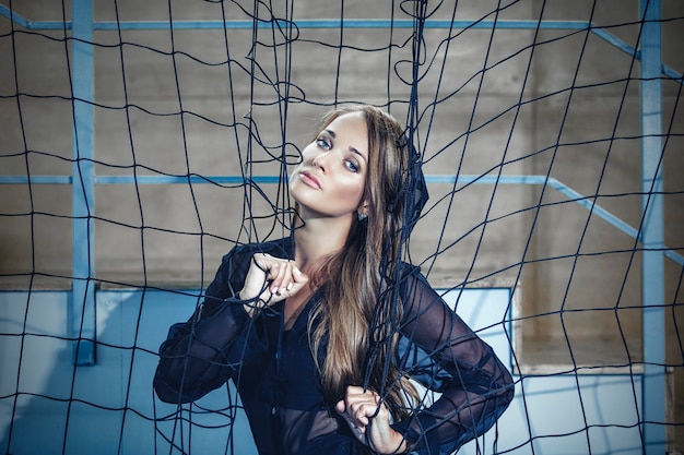 Photo beautiful young fashion model in a dress at a large sports stadium near the goal nets poses