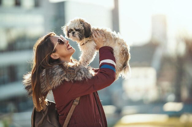 美しい若いファッションの女性は、街の通りで遊んでいる彼女のかわいいペットの犬と一緒に時間を過ごしています。