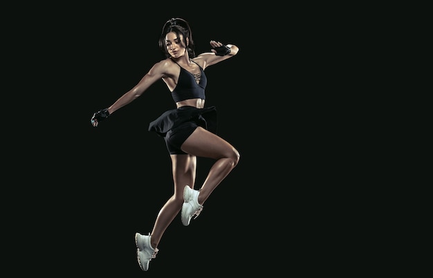 Beautiful young female athlete practicing on black background