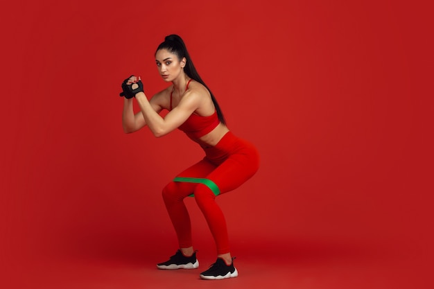 Beautiful young female athlete practicing on red  wall monochrome portrait