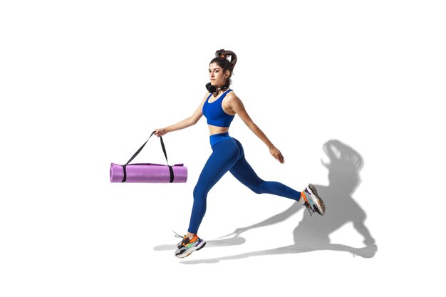 Beautiful young female athlete practicing on white studio background with shadows