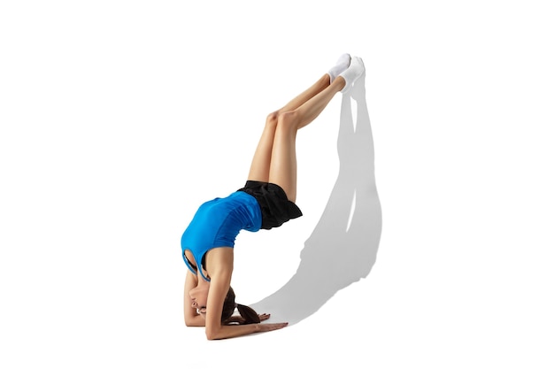 Beautiful young female athlete stretching on white studio background with shadows