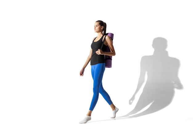 Beautiful young female athlete stretching on white studio background with shadows