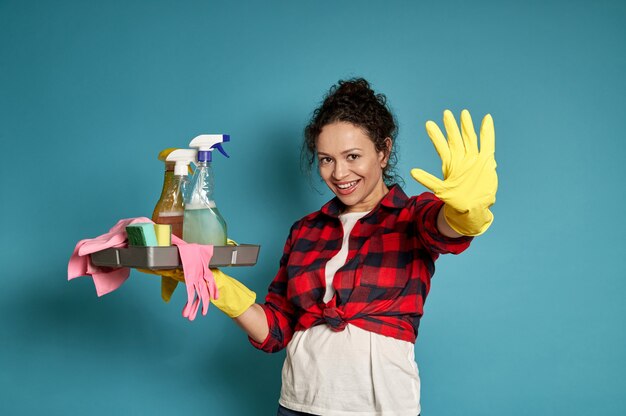 Beautiful young female cleaning contractor holding a bucket with cleaning products and gesturing STOP