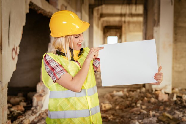 Beautiful young female construction architects in building damaged in the disaster. She is point to a blank white board and smiling.