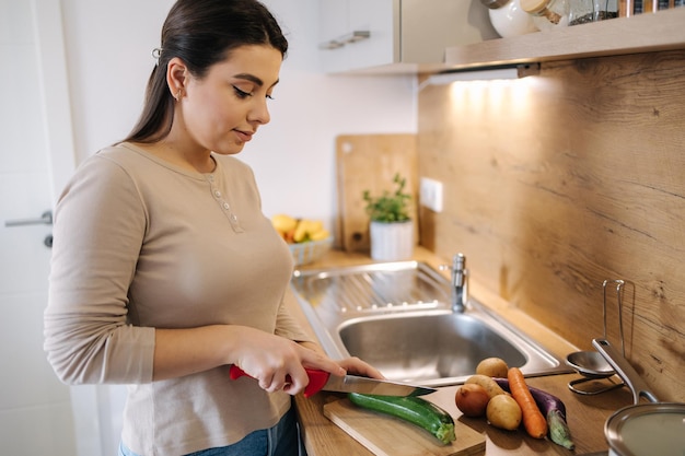 Beautiful young female cutting vegetables on kitchen at home Home food concept