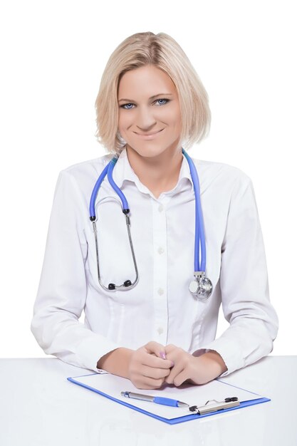 Beautiful young female doctor sitting near the table looking at camera smiling isolated