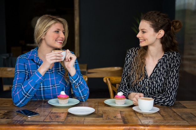 Beautiful young female friends having coffee while talking in cafeteria