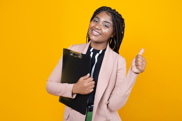 beautiful young female in a jacket with a folder on a yellow background with a hand gesture