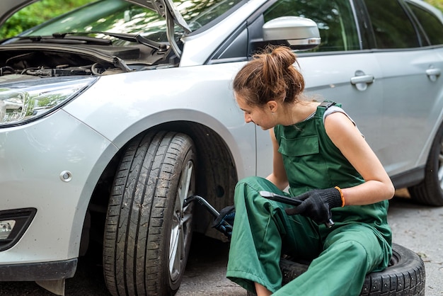 制服と特別なミトンの美しい若い女性のメカニックは、車の近くの仕事に完全に対応しますメカニックの女性のコンセプト車の修理のコンセプト