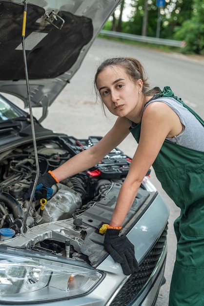 制服と特別なミトンの美しい若い女性のメカニックは、車の近くの仕事に完全に対応しますメカニックの女性のコンセプト車の修理のコンセプト