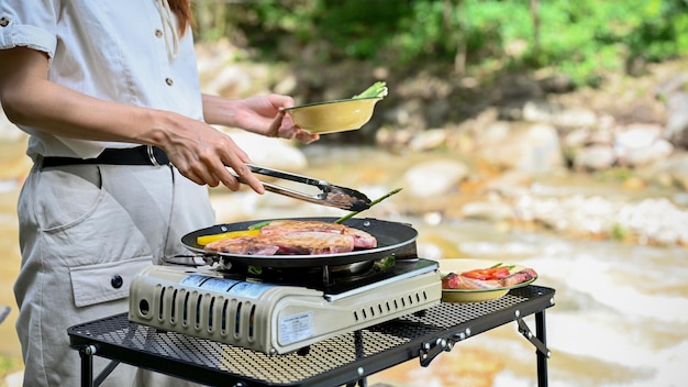 Bella giovane femmina che prepara barbecue all'aperto vicino al fiume che fa una bistecca di manzo