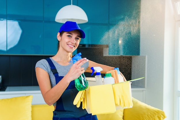 Beautiful young female professional cleaner in special uniform with headphones washing the floor with mop and listens to music at apartment.