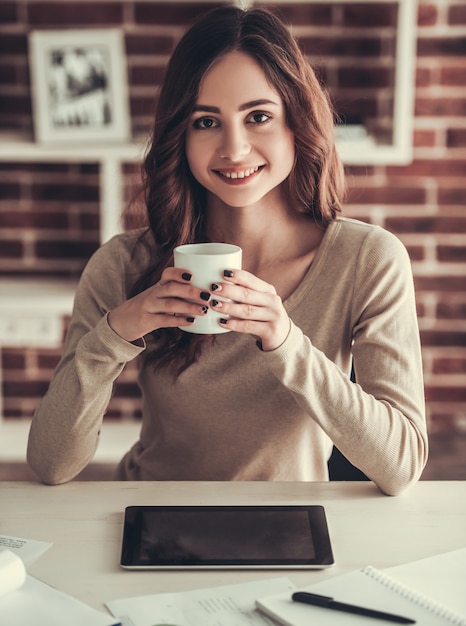 Beautiful young female student is holding a cup.