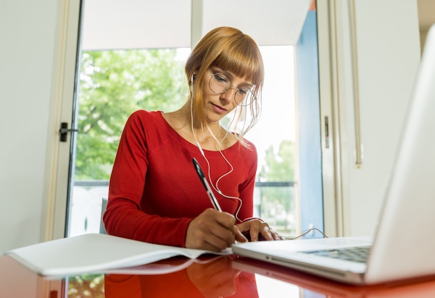 自宅のコンピューターで勉強して美しい若い女子学生。オンライン学校のコンセプト