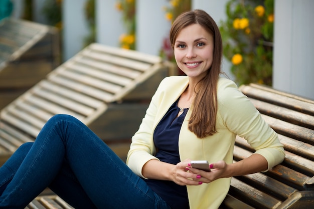 красивая молодая женщина летом на скамейке с мобильным телефоном