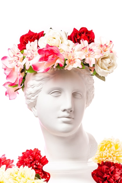 Beautiful young female white face and colorful flowers. Plaster antique bust of Venus in a floral wreath. Beauty spring and summer model girl with fresh bouquet.