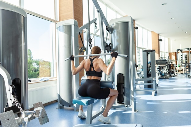 Bella giovane donna in forma che si allena su un pull down lat machine in palestra. vista posteriore