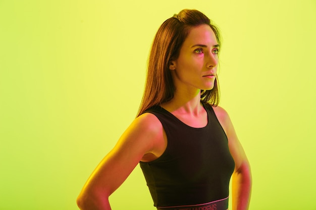 Beautiful young fitness girl standing isolated over blue wall, with hands on hips