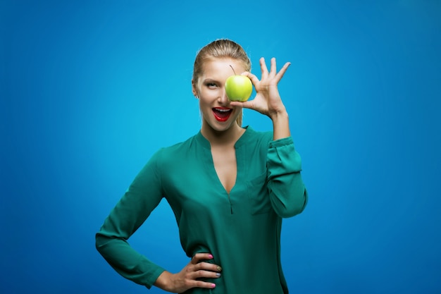 Красивая молодая женщина фитнеса счастливая улыбка держит зеленое яблоко. фото здорового образа жизни, изолированных на синей стене