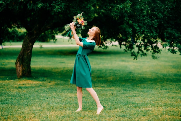 Beautiful young foxy girl in green elegant dress outdoor summer lifestyle portrait.  Pretty cheerful barefoot woman leisure at nature