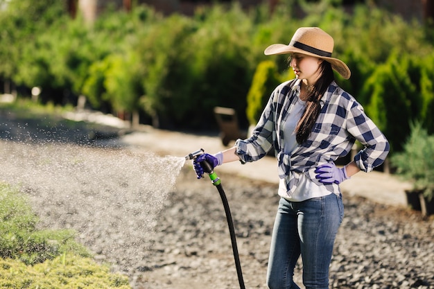 Beautiful young gardener woman watering garden in hot summer day.