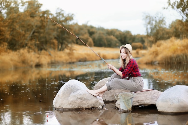 Красивая молодая девушка осенью у реки с удочкой