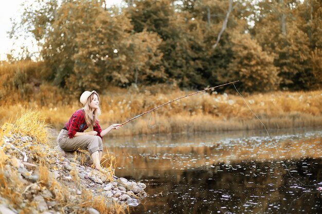 Beautiful young girl in autumn by the river with a fishing rod