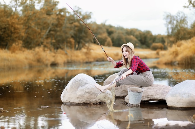 Beautiful young girl in autumn by the river with a fishing rod