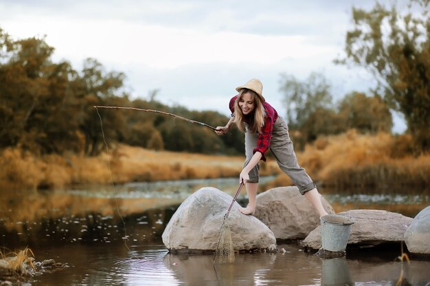 Beautiful young girl in autumn by the river with a fishing rod
