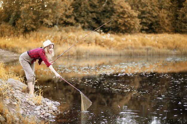 Beautiful young girl in autumn by the river with a fishing rod