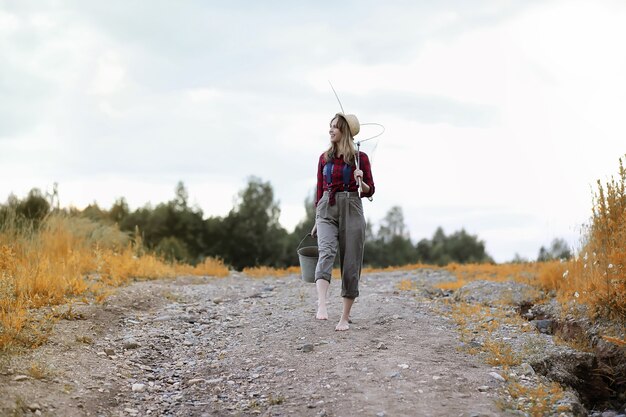 Beautiful young girl in autumn by the river with a fishing rod