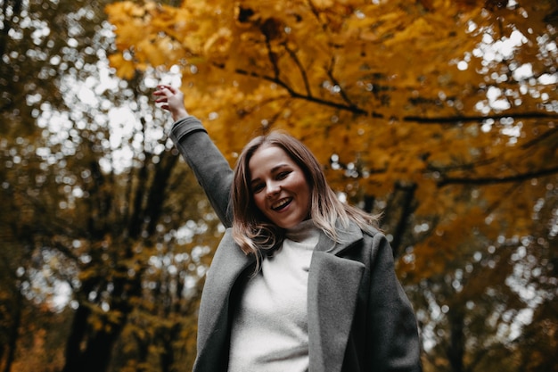 가을 공원에서 회색 코트를 입은 아름다운 소녀가 자연 속에서 사진 촬영을 위해 포즈를 취하고 있습니다.