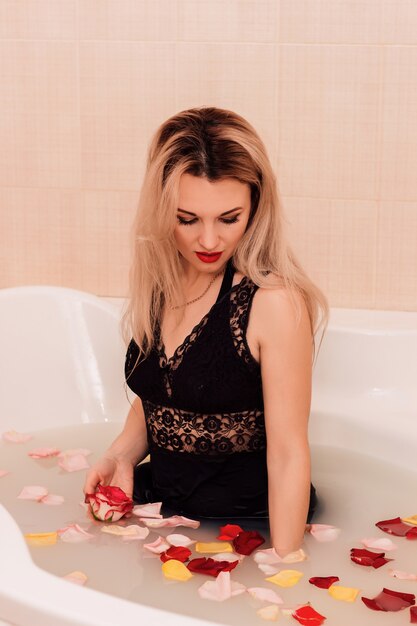 Beautiful young girl bathes in a bath with rose petals