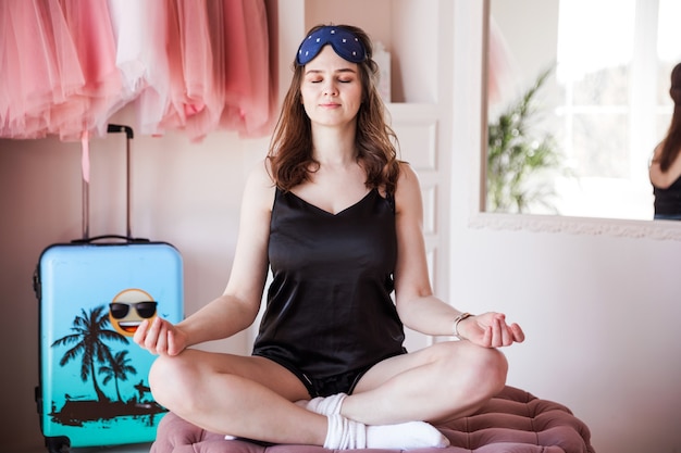 Beautiful young girl in black pajamas in the early morning practices yoga in her bedroom.  