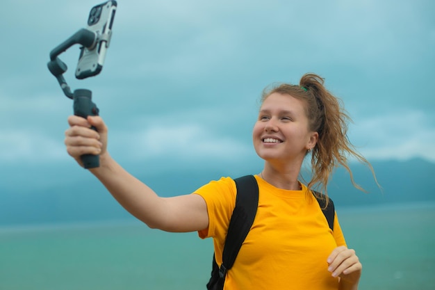 Beautiful young girl blogger outdoors walking traveling hikingholding stabilizer or gimbal with