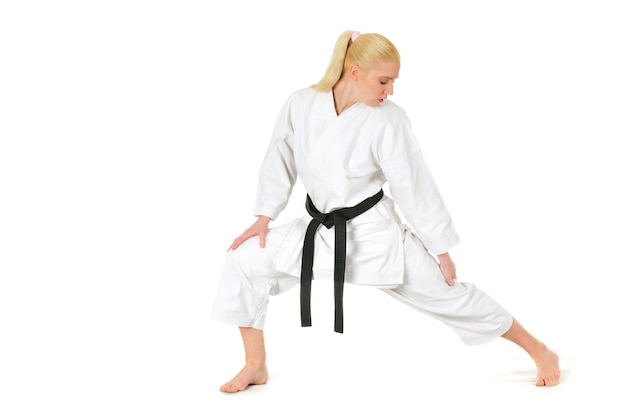 Beautiful young girl blonde karate sportswoman in a kimono makes a position to start workout. Professional sport concept. Place for advertising