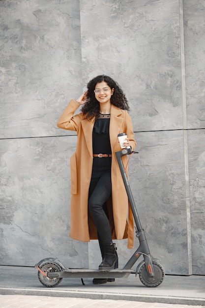 Beautiful young girl in a brown coat. Woman riding an electric scooter.