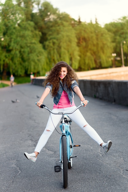 Beautiful young girl in casual clothes resting and cycling in the summer in the city along the embankment