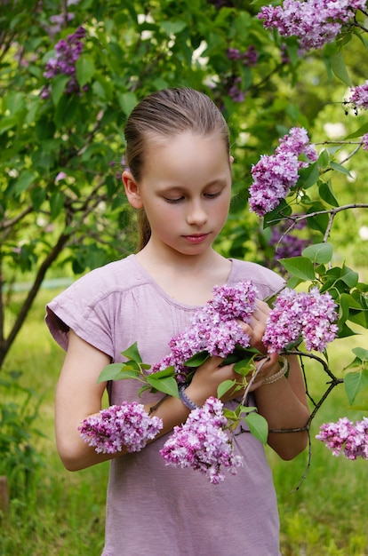 A beautiful young  girl child in the garden smelling lilac