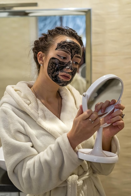 Beautiful young girl doing beauty treatments with black mask on face from acne