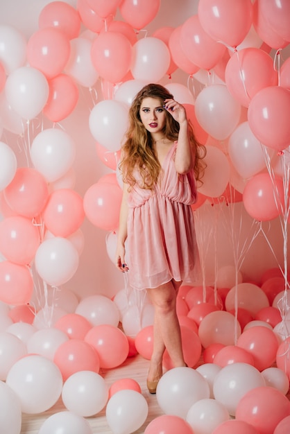 Beautiful young girl in a dress among a lot of pink balls.