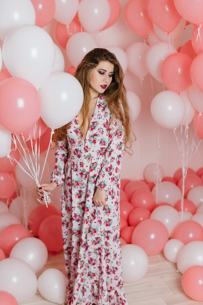 Beautiful young girl in a dress among a lot of pink balls.