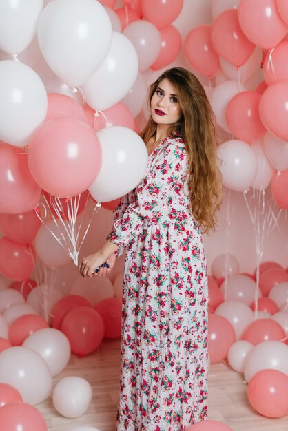 Beautiful young girl in a dress among a lot of pink balls.