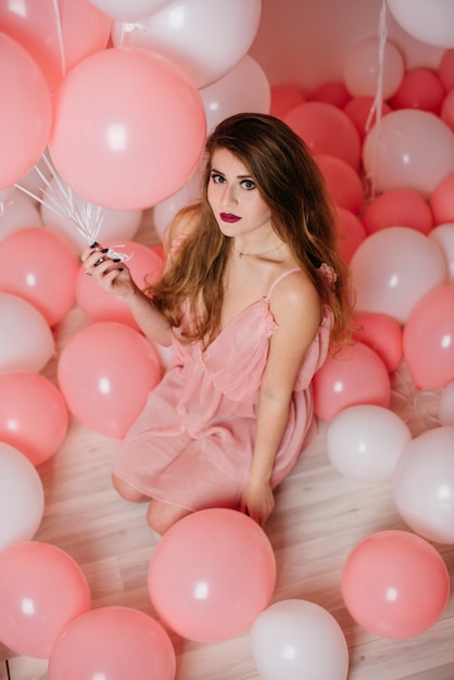 Beautiful young girl in a dress among a lot of pink balls.