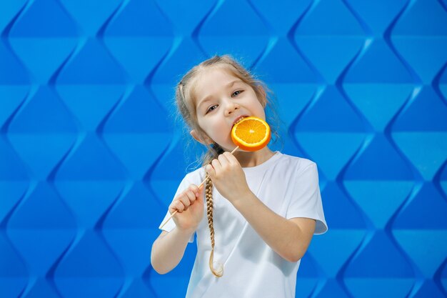 Beautiful young girl dressed in a white T-shirt holds half an orange in her hands and smiles. Orange fruits, she bites an orange and she likes.