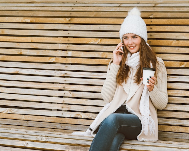 Beautiful young girl drinking coffee, tea from a plastic mug in autumn, winter and talking 